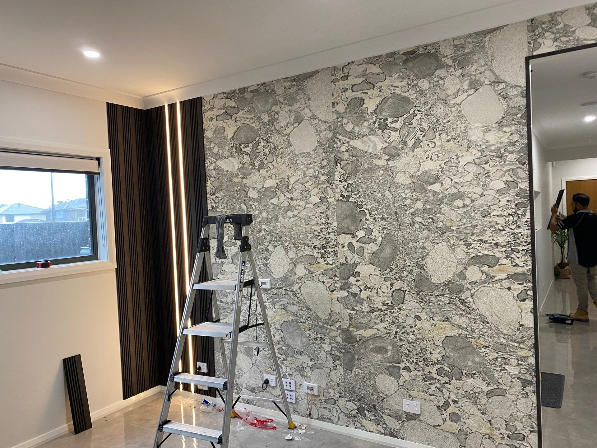 Room under renovation with a ladder and stone-textured feature wall beside a window.